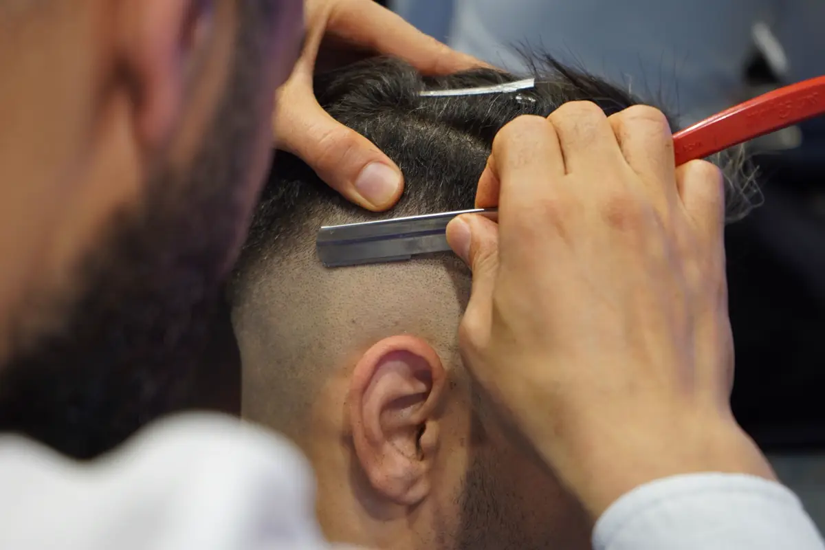Close-up: two hands setting the edge of a neckline with a straight razor.