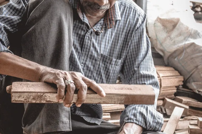 A joiner holding a cut board in the workshop, shavings on the bench.