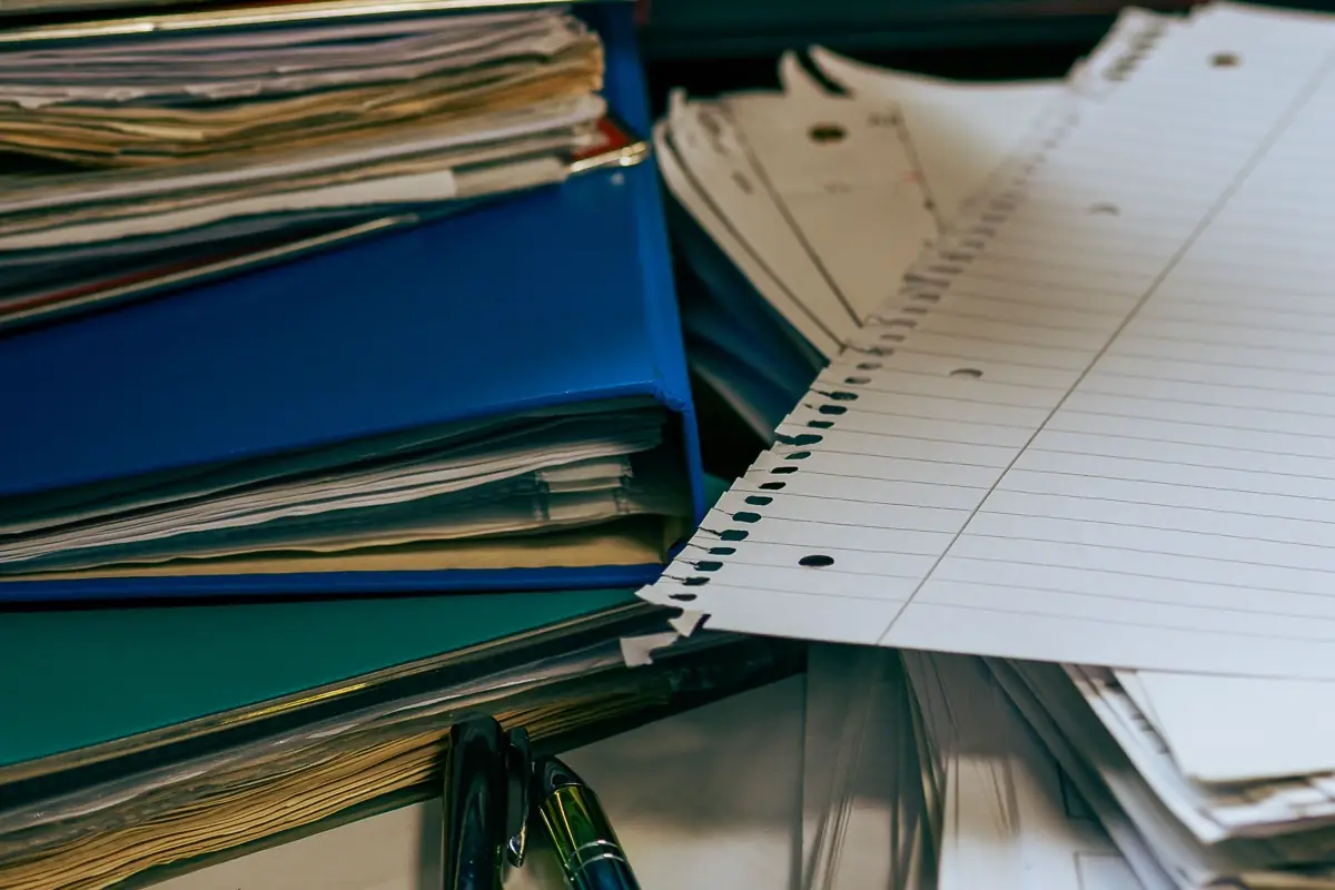 A stack of full ring binders and loose paperwork on a desk.