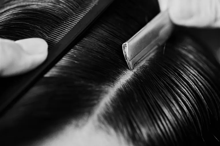 A comb drawing a sharp parting through dark wet hair.