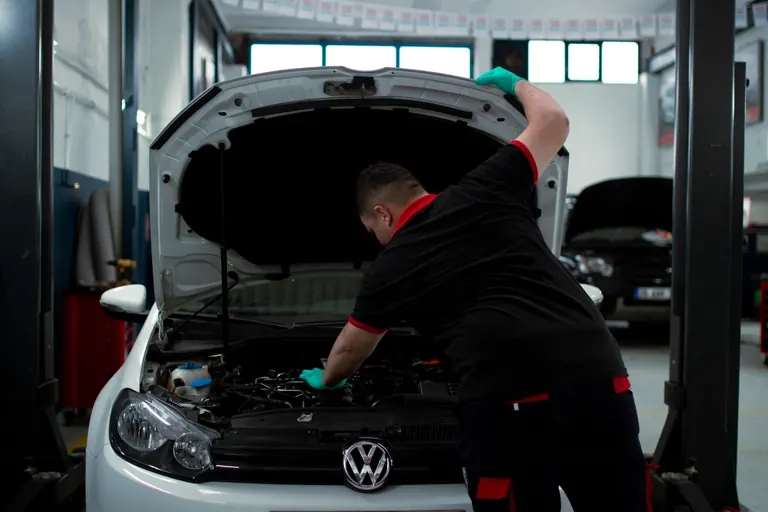 A mechanic leaning over the open engine bay of a car in a workshop.